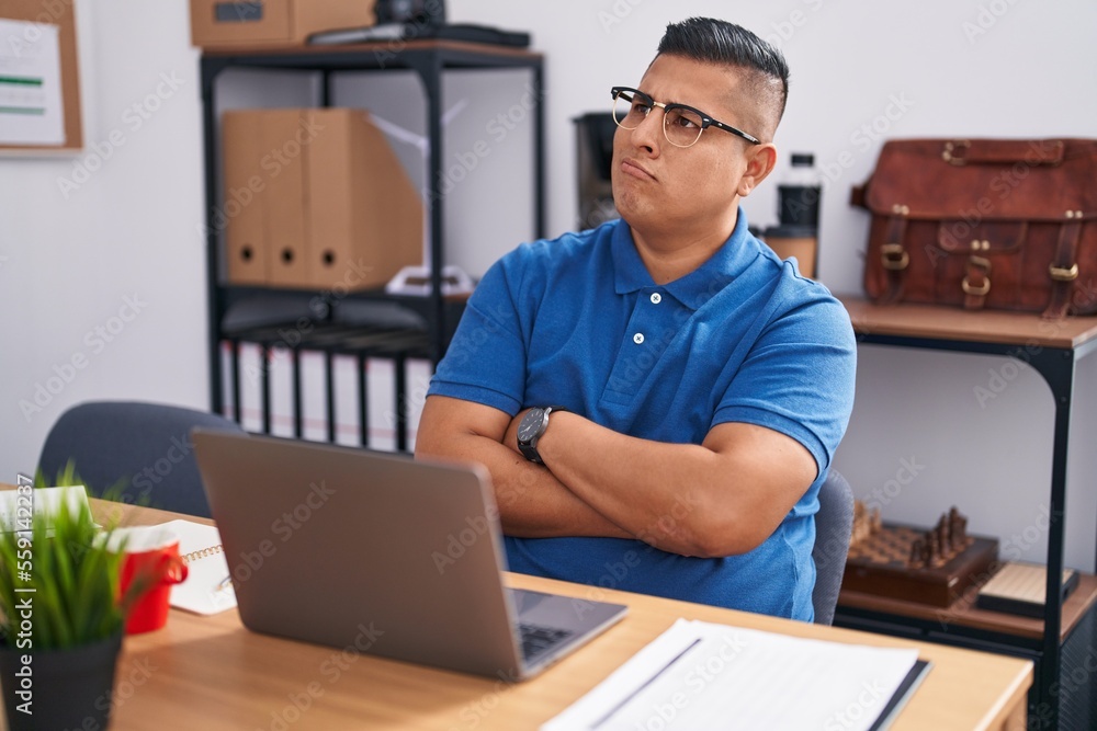 Young hispanic man working at the office with laptop smiling looking to the side and staring away thinking.