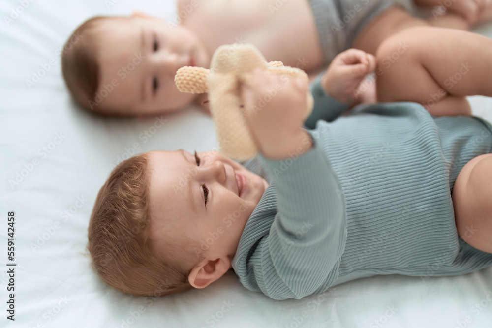 Two toddlers lying on bed playing with teddy bear at bedroom Two toddlers lying on bed playing with teddy bear at bedroom