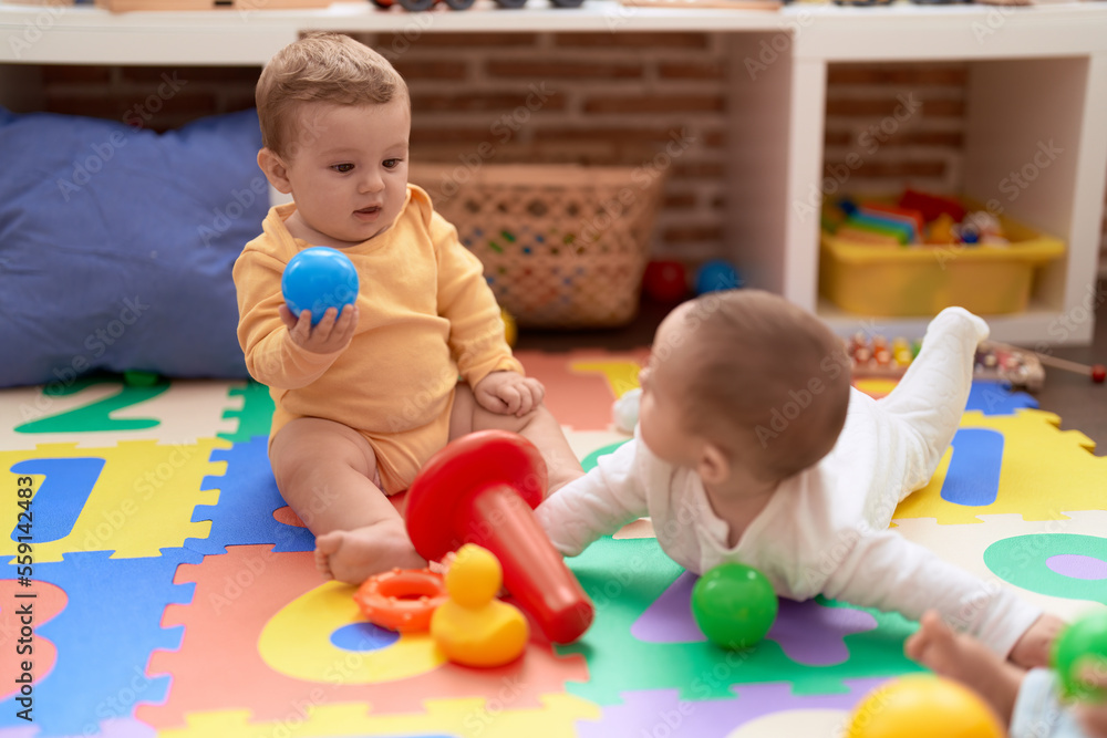 Two toddlers playing with balls sitting on floor at kindergarten Two toddlers playing with balls sitting on floor at kindergarten