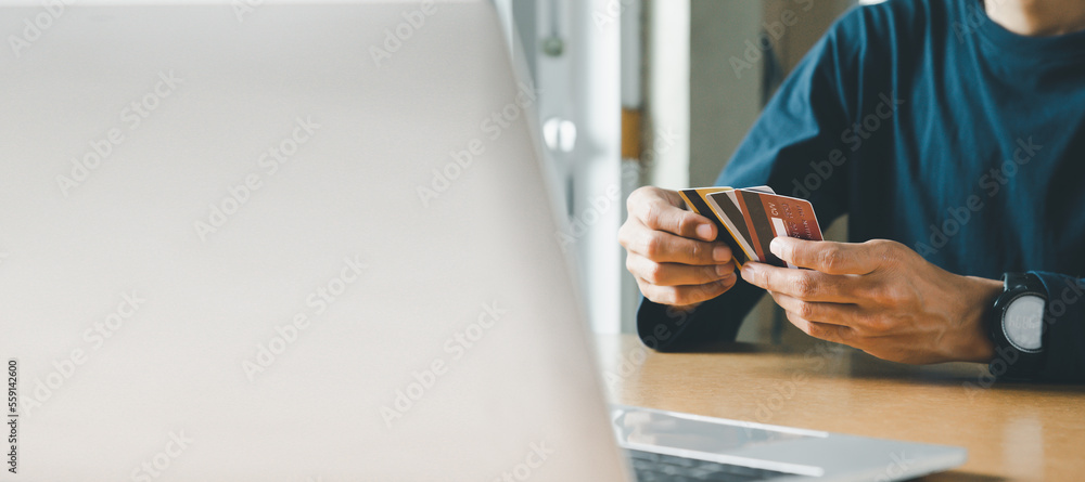 Naklejka premium Man hand holding credit card and using laptop at home, Businessman or entrepreneur working, Online shopping, e-commerce, internet banking, spending money concept.