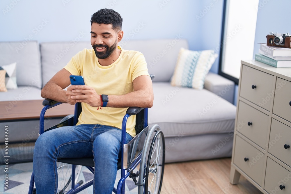 Young arab man using smartphone sitting on wheelchair at home