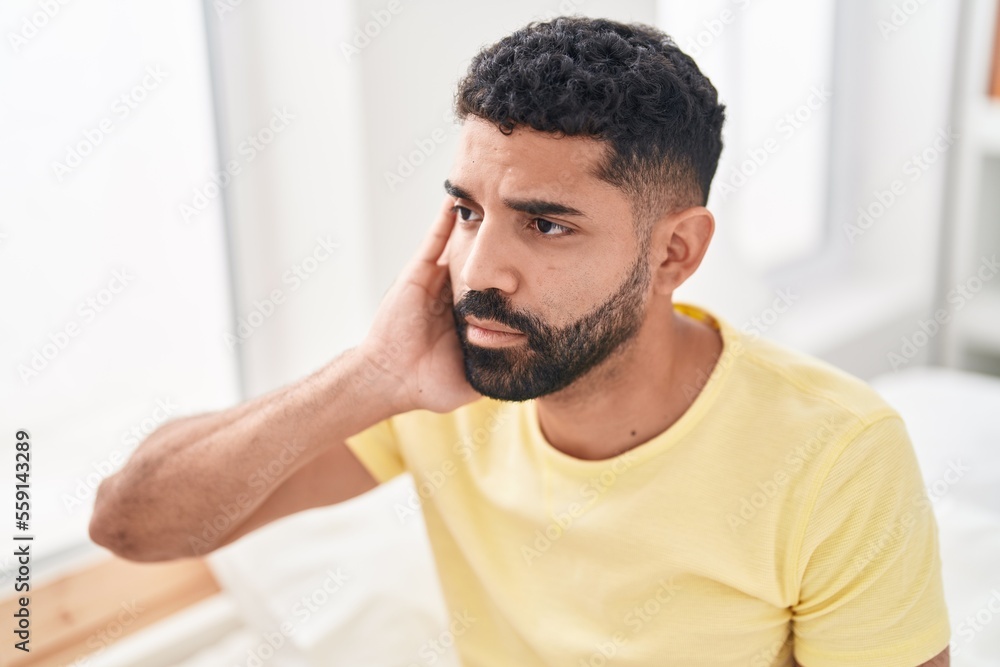 Young arab man suffering for ear pain sitting on bed at bedroom Young arab man suffering for ear pain sitting on bed at bedroom