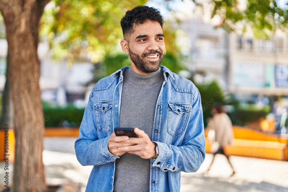 Fototapeta premium Young hispanic man smiling confident using smartphone at park