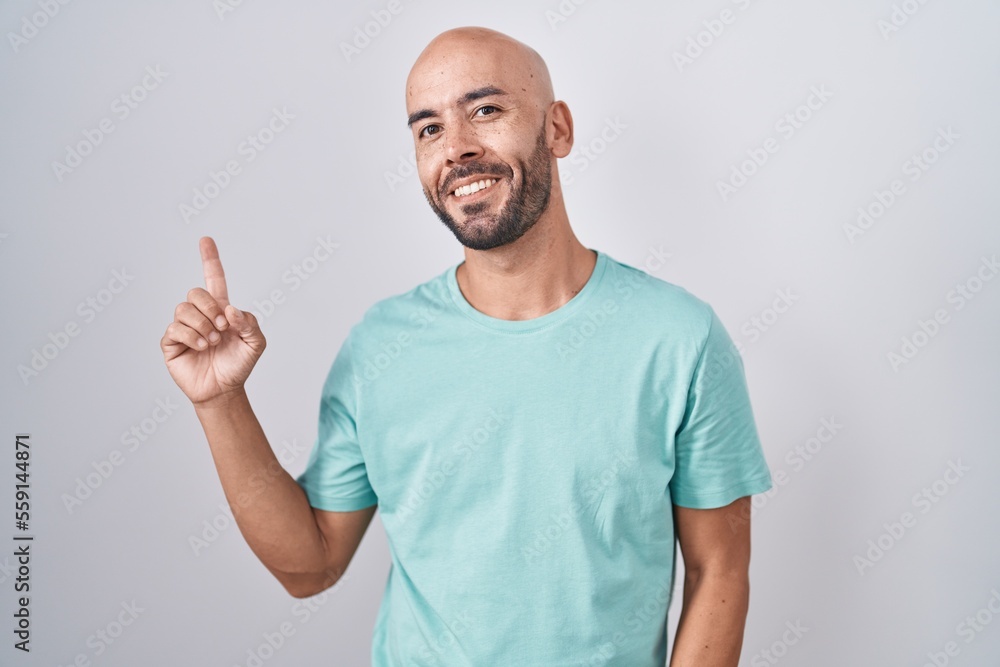 Middle age bald man standing over white background with a big smile on face, pointing with hand finger to the side looking at the camera. Middle age bald man standing over white background with a big smile on face, pointing with hand finger to the side looking at the camera.