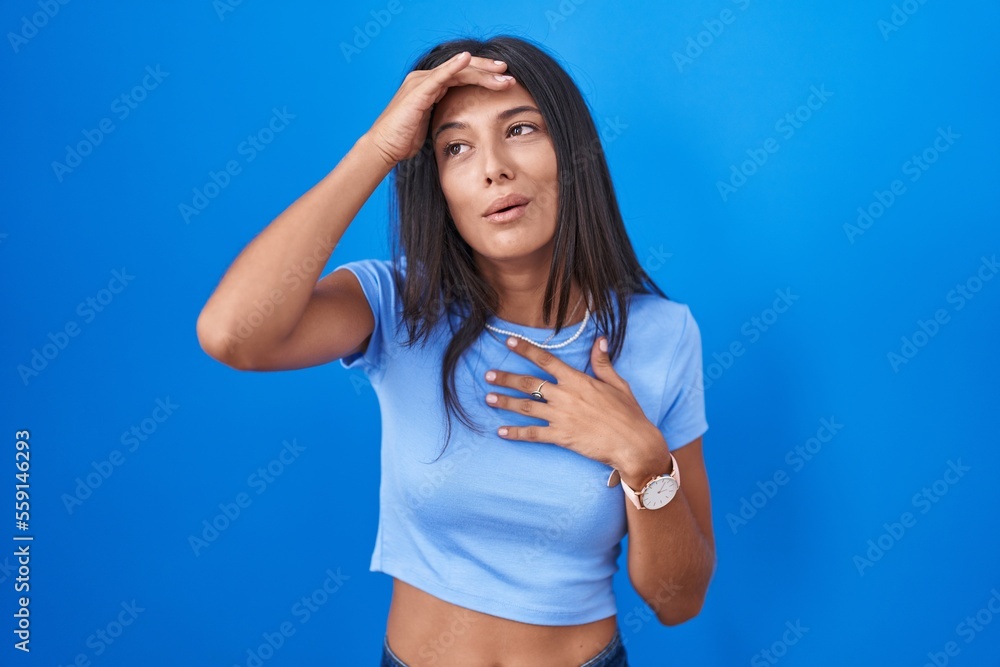 Brunette young woman standing over blue background touching forehead for illness and fever, flu and cold, virus sick Brunette young woman standing over blue background touching forehead for illness and fever, flu and cold, virus sick