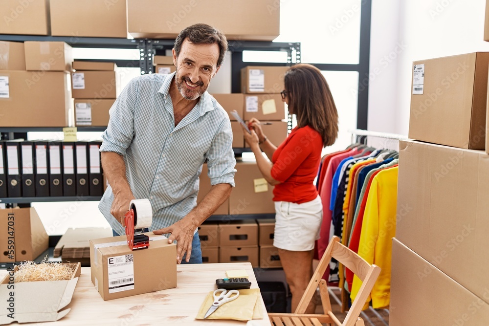 Middle age man and woman business partners smiling confident packing package at storehouse Middle age man and woman business partners smiling confident packing package at storehouse