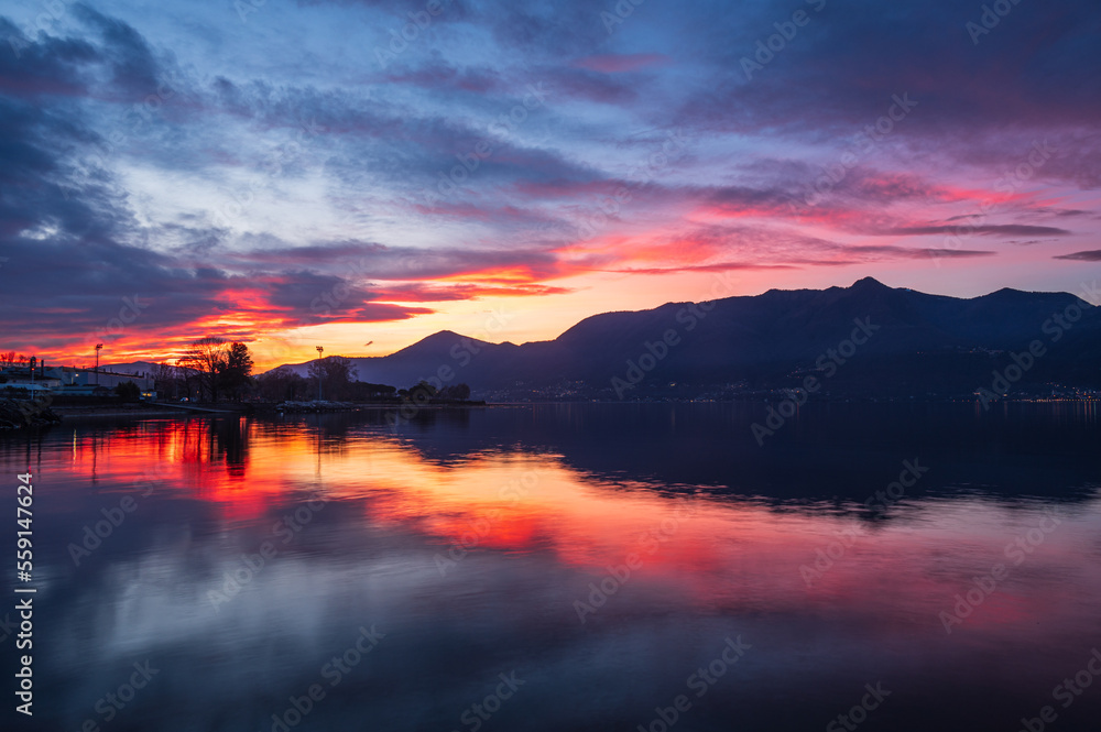 Beautiful colorful sunset with clouds and mountains reflecting on Lake Maggiore in Luino Beautiful colorful sunset with clouds and mountains reflecting on Lake Maggiore in Luino