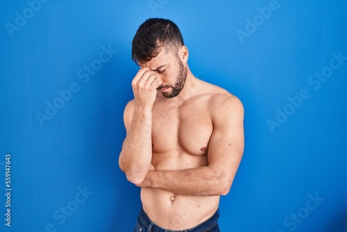 Handsome hispanic man standing shirtless tired rubbing nose and eyes feeling fatigue and headache. stress and frustration concept.