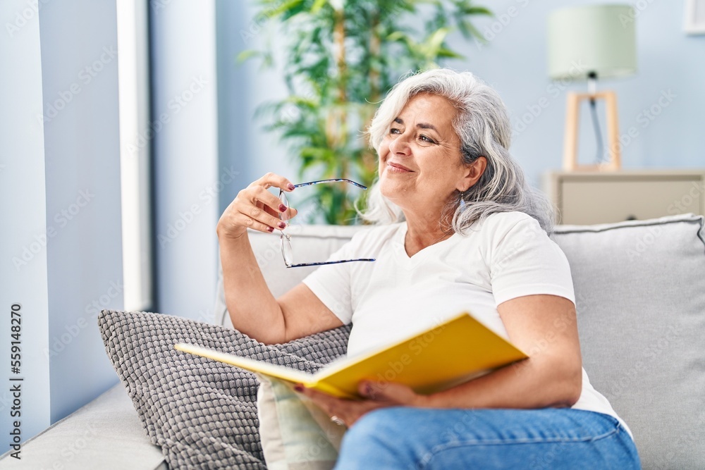 Middle age woman reading book sitting on sofa at home Middle age woman reading book sitting on sofa at home