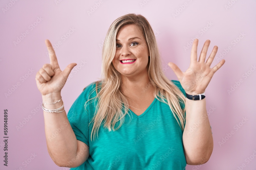 Fototapeta premium Caucasian plus size woman standing over pink background showing and pointing up with fingers number seven while smiling confident and happy.