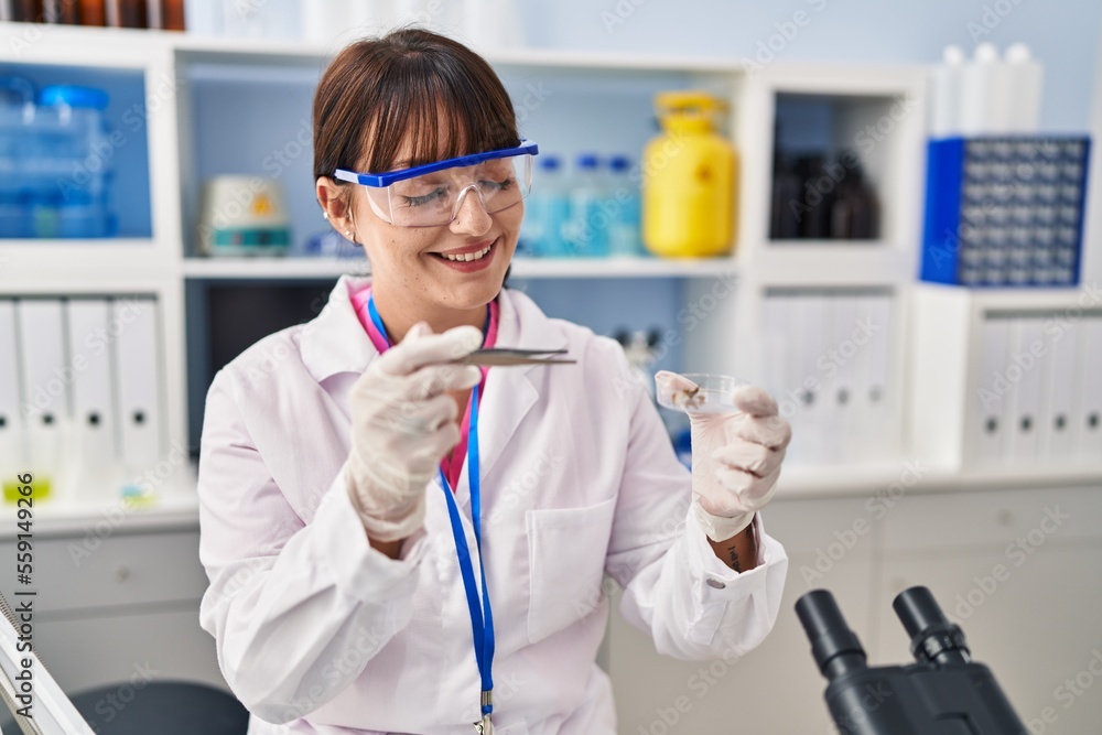 Young beautiful hispanic woman scientist smiling confident holding plant sample and tweezers at pharmacy Young beautiful hispanic woman scientist smiling confident holding plant sample and tweezers at pharmacy