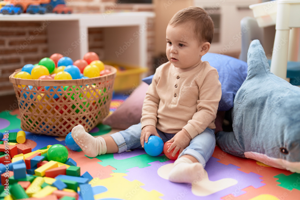 Adorable toddler playing with balls sitting on floor at kindergarten Adorable toddler playing with balls sitting on floor at kindergarten