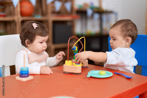 Two toddlers playing with toys sitting on table at kindergarten