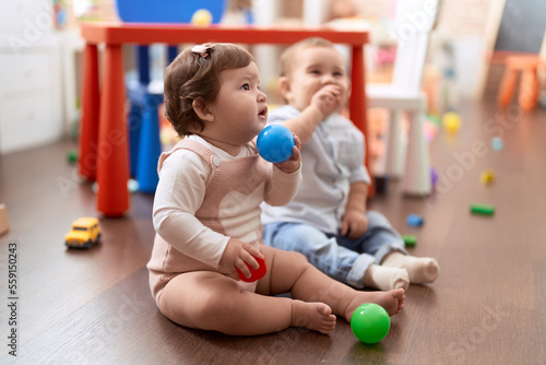 Two toddlers playing with balls sitting on floor at kindergarten
