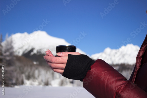 A young woman holds a cup of tea against the background of mountains in winter. Strbske Pleso Lake, Slovakia