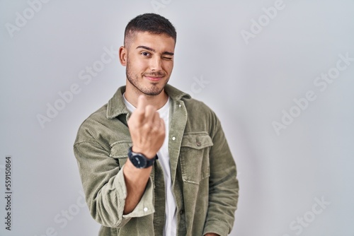 Young hispanic man standing over isolated background beckoning come here gesture with hand inviting welcoming happy and smiling © Krakenimages.com