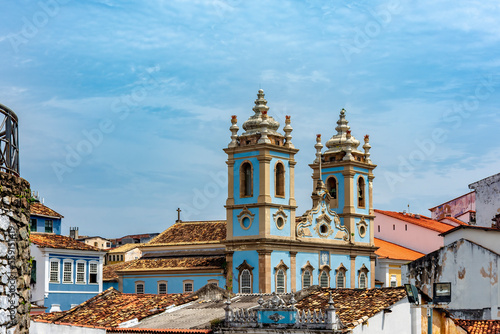 Tower and facade of a historic baroque church emerging from among the houses and roofs of the Pelourinho district, city of Salvador, Bahia