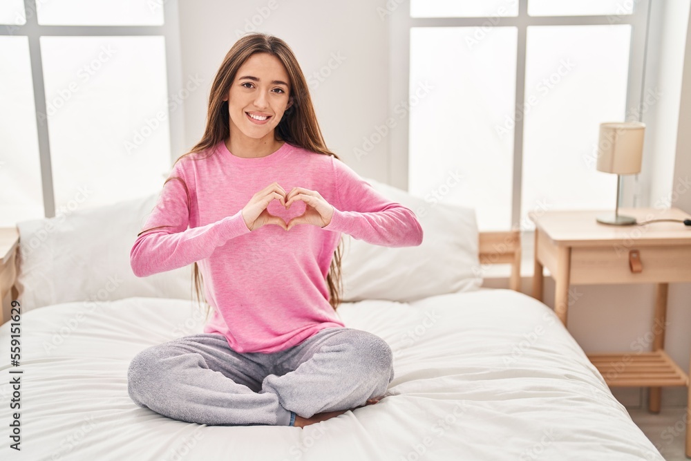Young beautiful hispanic woman doing heart gesture sitting on bed at bedroom Young beautiful hispanic woman doing heart gesture sitting on bed at bedroom