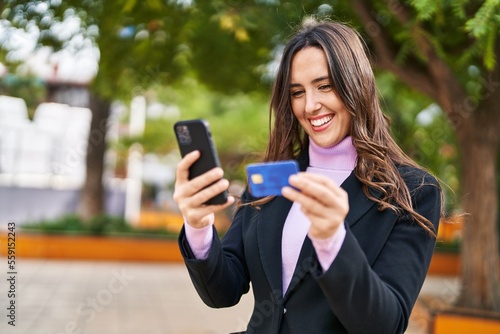 Young hispanic woman using smartphone and credit card at park