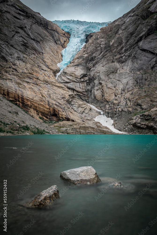 Briksdalsbreen glacier ice in the mountains of Jostedalsbreen national park in Norway, rocks in the water of turquoise glacier lake