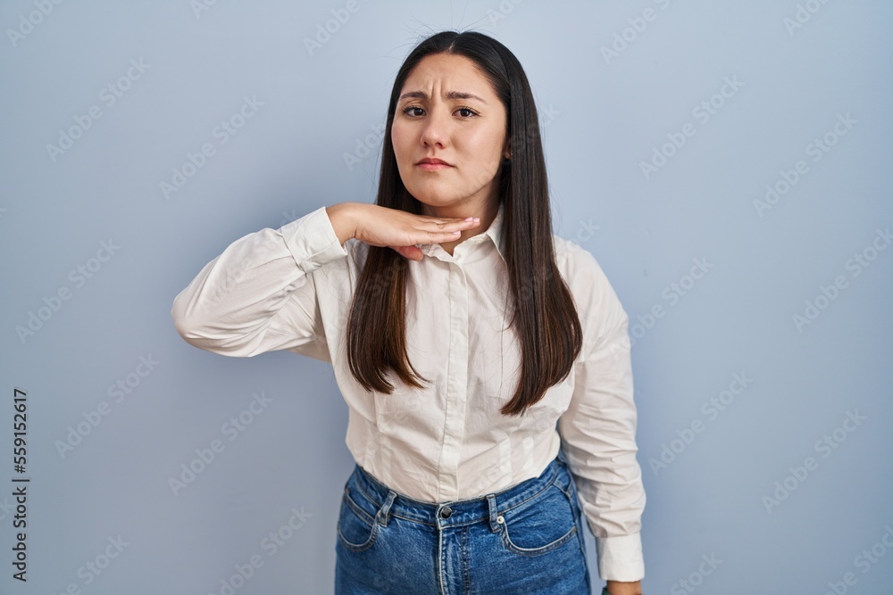 Young latin woman standing over blue background cutting throat with hand as knife, threaten aggression with furious violence Young latin woman standing over blue background cutting throat with hand as knife, threaten aggression with furious violence