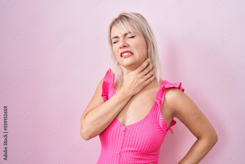 Young caucasian woman standing over pink background touching painful neck, sore throat for flu, clod and infection Young caucasian woman standing over pink background touching painful neck, sore throat for flu, clod and infection