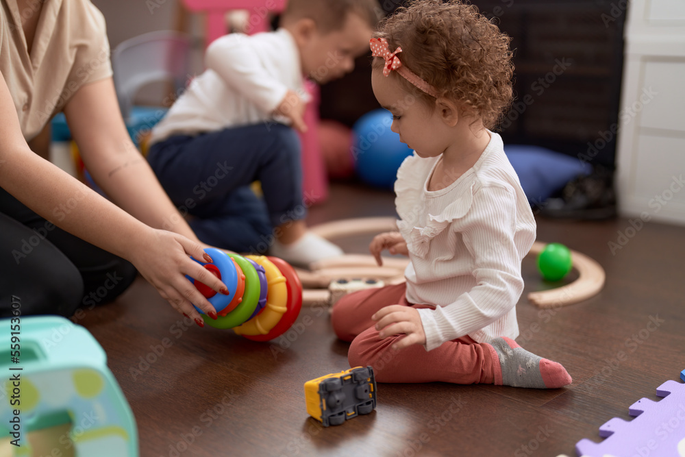 Fototapeta premium Adorable girl and boy playing with hoops sitting on floor at kindergarten