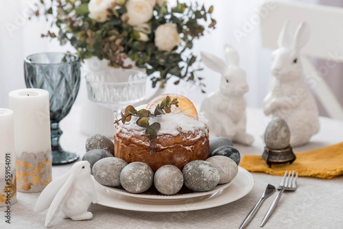 Spring table setting. A plate with a cotton napkin with a bunny, a cake and Easter eggs. Silverware, Easter bunnies and a vase of flowers on a linen tablecloth. The concept of a bright Easter holiday.