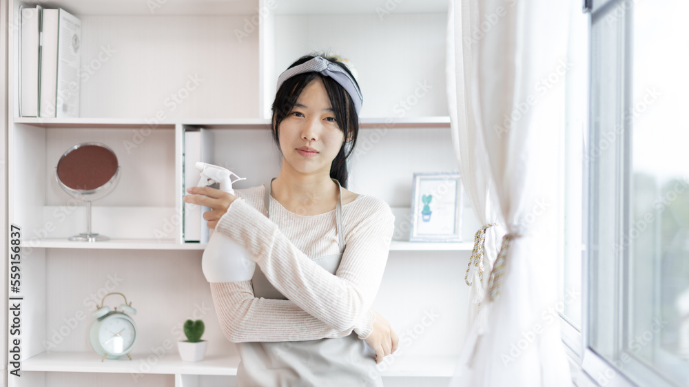 Young housewife holding a spray bottle to clean things in the living room, Big cleaning, Housework, Daily routine ,Removes germs and dirt and deep stains, Spray alcohol, Clean up. Young housewife holding a spray bottle to clean things in the living room, Big cleaning, Housework, Daily routine ,Removes germs and dirt and deep stains, Spray alcohol, Clean up.
