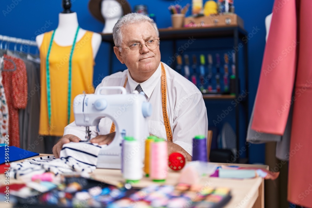 Middle age grey-haired man tailor using sewing machine at tailor shop Middle age grey-haired man tailor using sewing machine at tailor shop