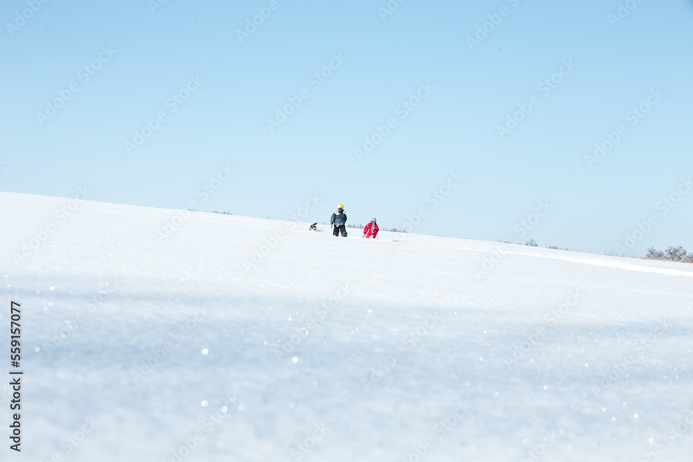 Two silhouettes of children in blue and red overalls against a clear blue sky. People on the horizon. The children went into the distance on clear white snow. .Soft focus. Blured. Film Grain Defocused