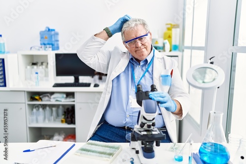 Senior caucasian man working at scientist laboratory confuse and wondering about question. uncertain with doubt  thinking with hand on head. pensive concept.