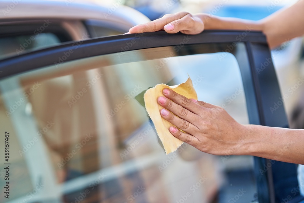 Obraz premium Young beautiful hispanic woman cleaning glass window car at street