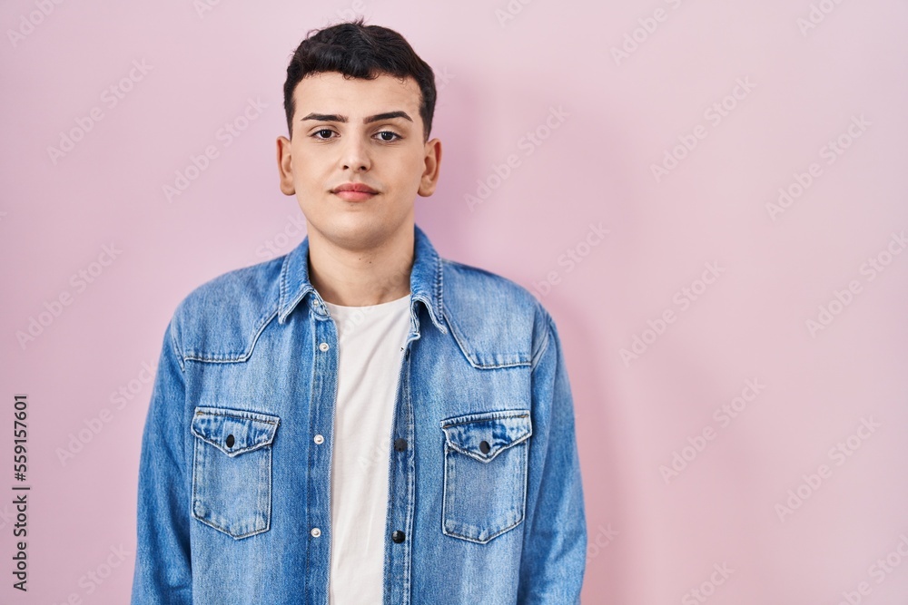 Non binary person standing over pink background with serious expression on face. simple and natural looking at the camera. Non binary person standing over pink background with serious expression on face. simple and natural looking at the camera.