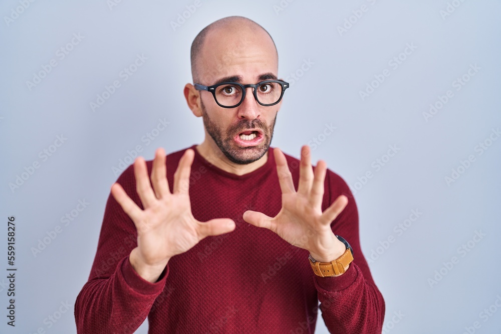 Naklejka premium Young bald man with beard standing over white background wearing glasses afraid and terrified with fear expression stop gesture with hands, shouting in shock. panic concept.
