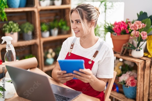 Young blonde woman florist smiling confident using laptop and touchpad at flower shop