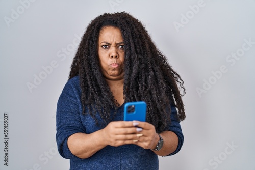 Plus size hispanic woman using smartphone typing message skeptic and nervous, frowning upset because of problem. negative person.