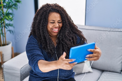 African american woman watching video on touchpad sitting on sofa at home
