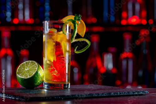 Cocktail iced tea with ice on bar counter in a restaurant, pub. Orange drink with juice. Fresh prepared alcoholic cooler beverage at nightclub. Showcases with bottles on dark background