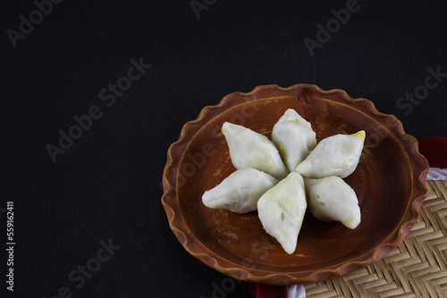 makar sangkranti or poush sangkranti celebration with puli pithe or bengali rice flour dumplings with coconut fillings served on a clay plate with jaggery. shot against black background. photo