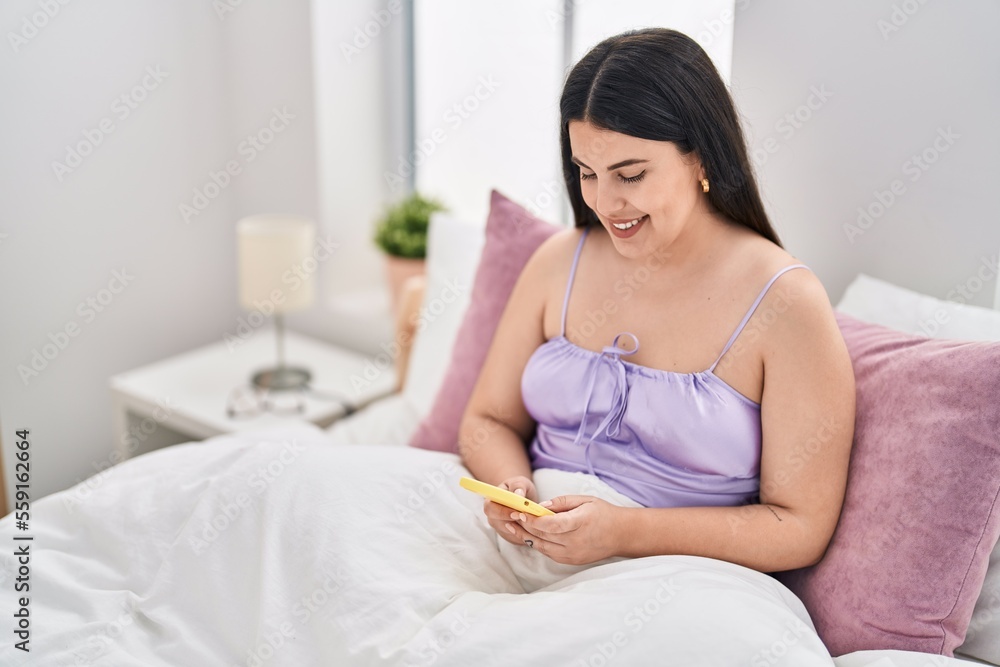 Young hispanic woman using smartphone sitting on bed at bedroom Young hispanic woman using smartphone sitting on bed at bedroom