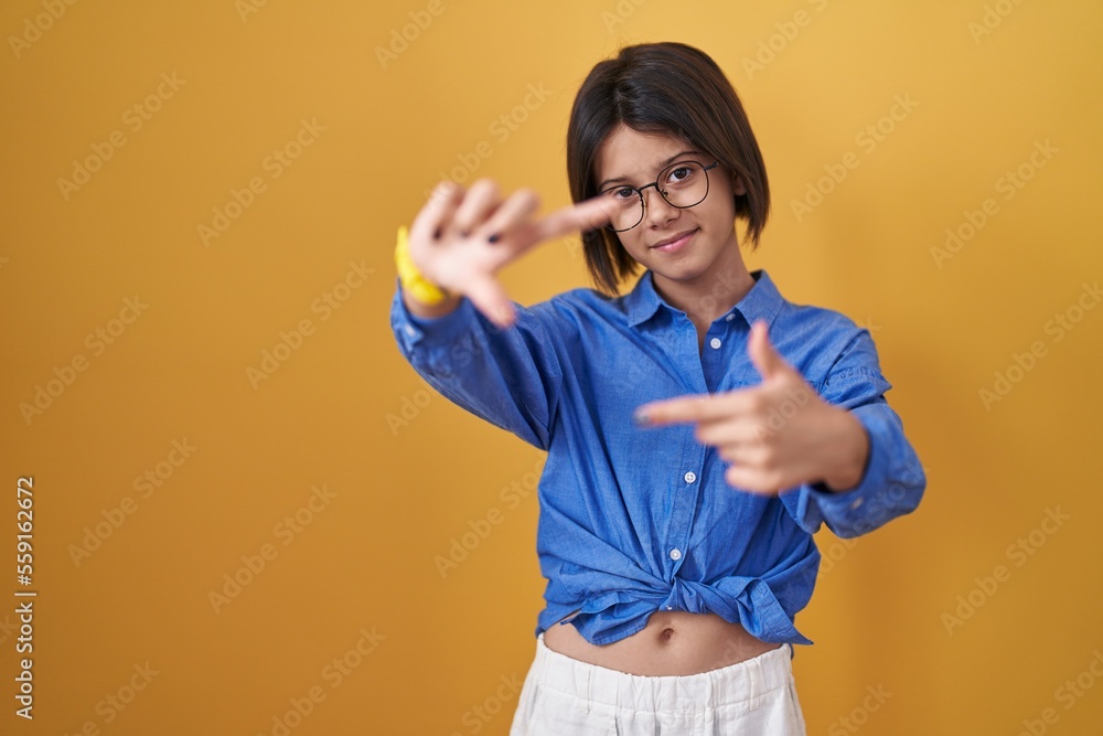 Young girl standing over yellow background smiling making frame with hands and fingers with happy face. creativity and photography concept. Young girl standing over yellow background smiling making frame with hands and fingers with happy face. creativity and photography concept.
