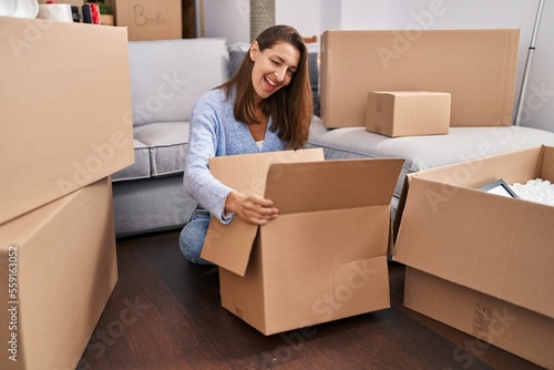 Young woman moving to a new home looking inside cardboard box winking looking at the camera with sexy expression  cheerful and happy face.
