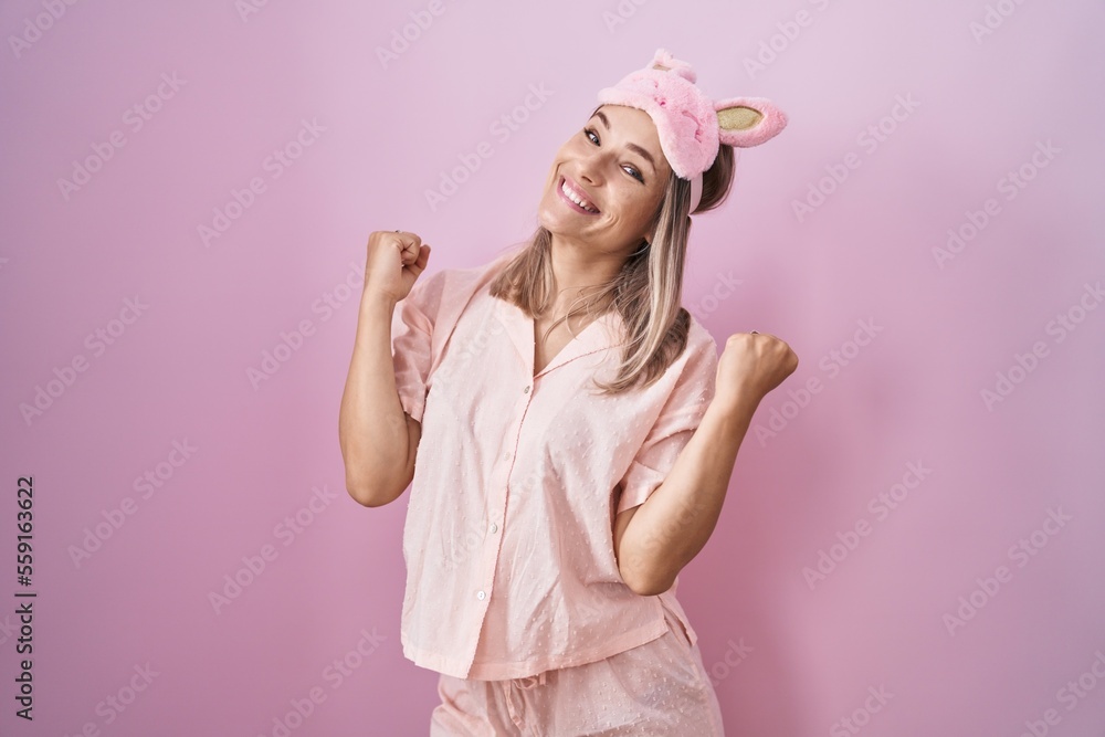 Blonde caucasian woman wearing sleep mask and pajama celebrating surprised and amazed for success with arms raised and eyes closed. winner concept.