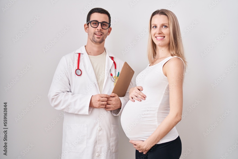Young woman expecting a baby with doctor looking positive and happy standing and smiling with a confident smile showing teeth Young woman expecting a baby with doctor looking positive and happy standing and smiling with a confident smile showing teeth