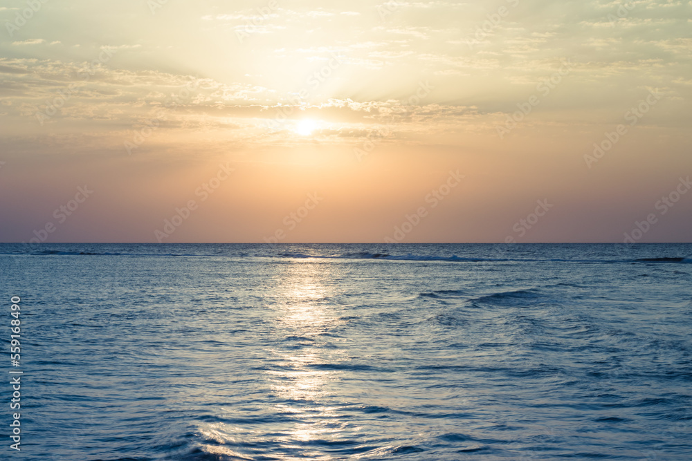 Beautiful sunrise at sea. Dawn on the Red Sea. The sun is reflected in the sea. Light clouds in the blue dawn sky. Tropical sunrise.