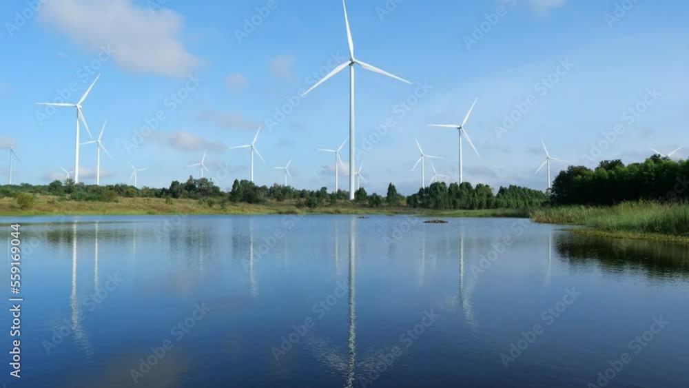 Time Lapse of Powerful Wind turbine farm for pure energy production on Beautiful clear blue sky with white clouds and wind turbine farm reflection on lake. renewable energy. Hyperlapse View Time Lapse of Powerful Wind turbine farm for pure energy production on Beautiful clear blue sky with white clouds and wind turbine farm reflection on lake. renewable energy. Hyperlapse View