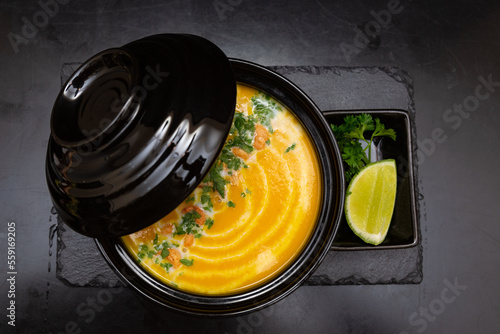 pumpkin soup in a black plate, on a black wooden background next to a slice of lemon
