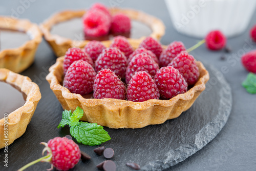 Delicious tart with chocolate cream and fresh raspberry on a gray background. Summer dessert. Copy space.