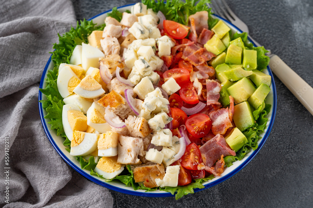 Tradition Cobb salad with fried chicken, avocado, fresh tomatoes, eggs, bacon and cheese on a plate on a dark background. Top view, copy space, selective focus Tradition Cobb salad with fried chicken, avocado, fresh tomatoes, eggs, bacon and cheese on a plate on a dark background. Top view, copy space, selective focus